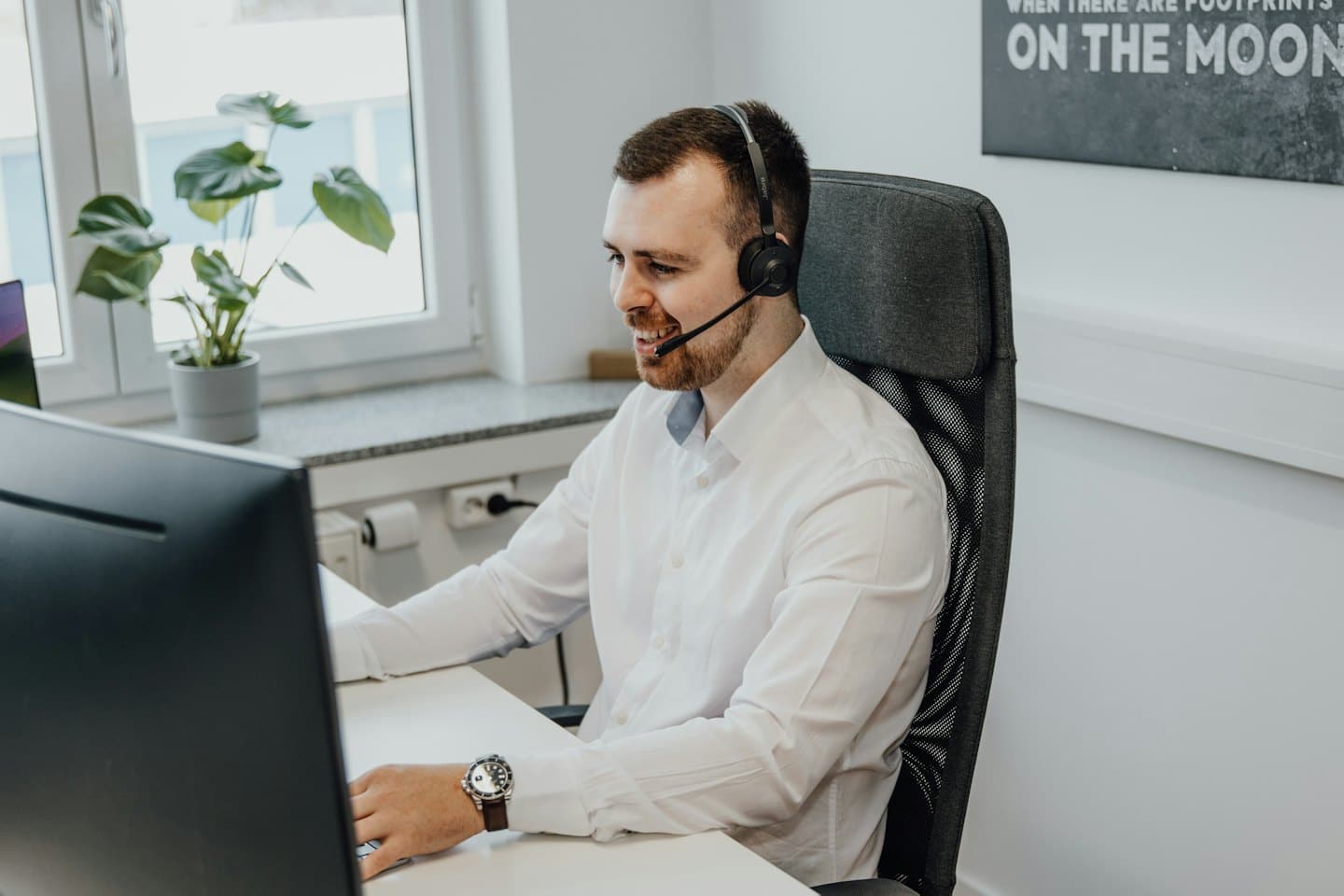 Un homme souriant avec un casque travaille sur un ordinateur.