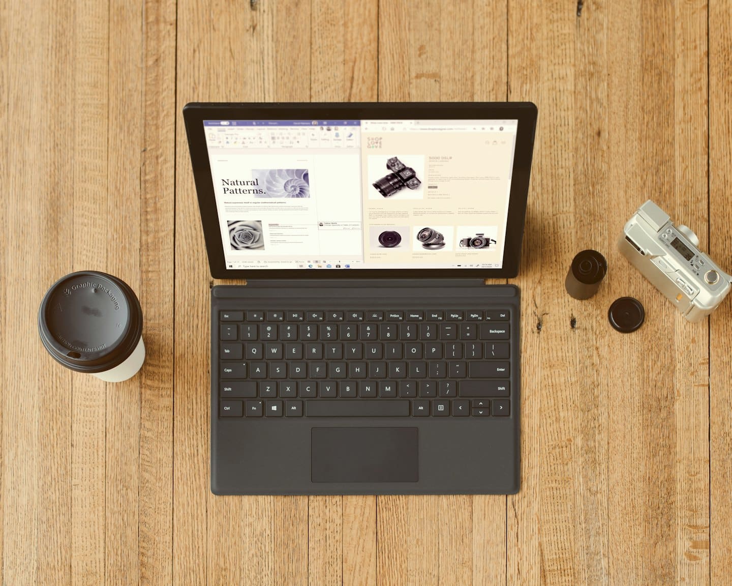 Ordinateur portable, tasse de café et appareil photo disposés sur un bureau en bois.